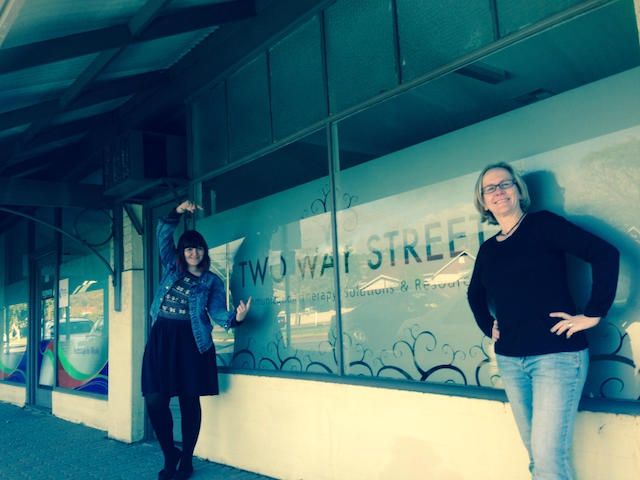 Photo of the Two Way Street office frontage with two smiling staff members standing outside pointing to the sign.