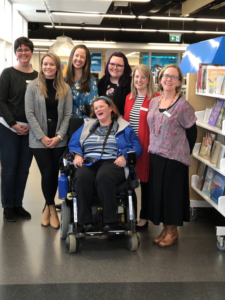 Photo of 7 smiling Two Way Street staff members in a library