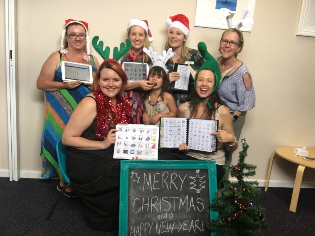 Picture of 6 of the Two Way Street team, with Janelle's daughter wearing Christmas hats, holding various communication tools with a blackboard sign saying Merry Christmas and a happy new year.