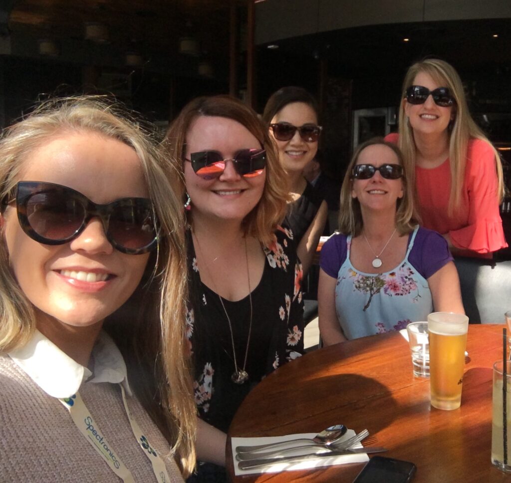 Photo of 5 Two Way Street staff members all wearing sunglasses, sitting at a table of a restaurant, smiling at the camera
